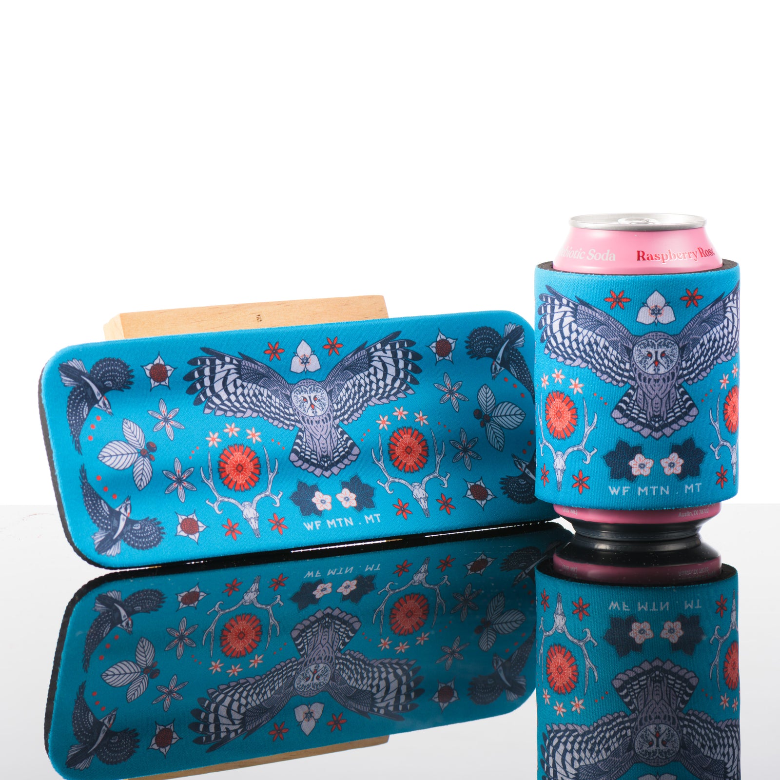 This blue slap can cooler is featuring artwork inspired by whitefish Mountain in Montana. The central motif is an owl.