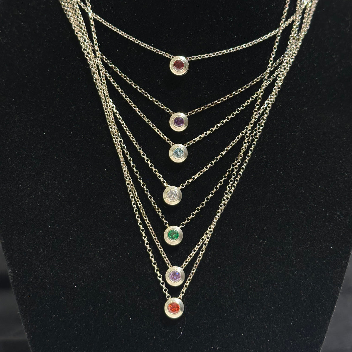 Seven necklaces with different colored cubic zirconia birthday stones inlayed on a black background