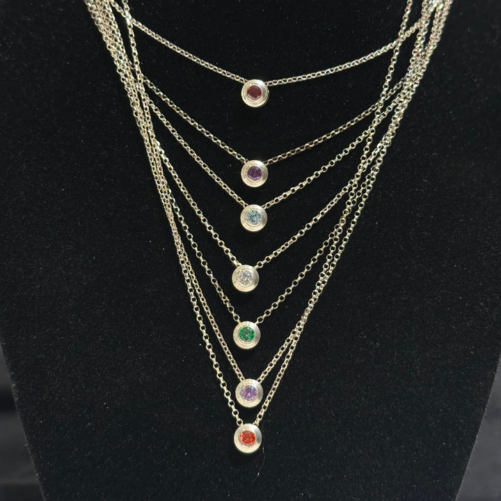 Seven necklaces with different colored cubic zirconia birthday stones inlayed on a black background