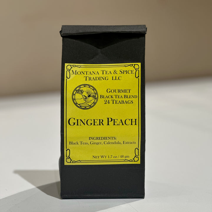 A black stand-up pouch of Montana Tea &amp; Spice Trading, LLC Gourmet Black Tea Blend Ginger Peach, featuring a bright yellow label, set against a neutral beige background.