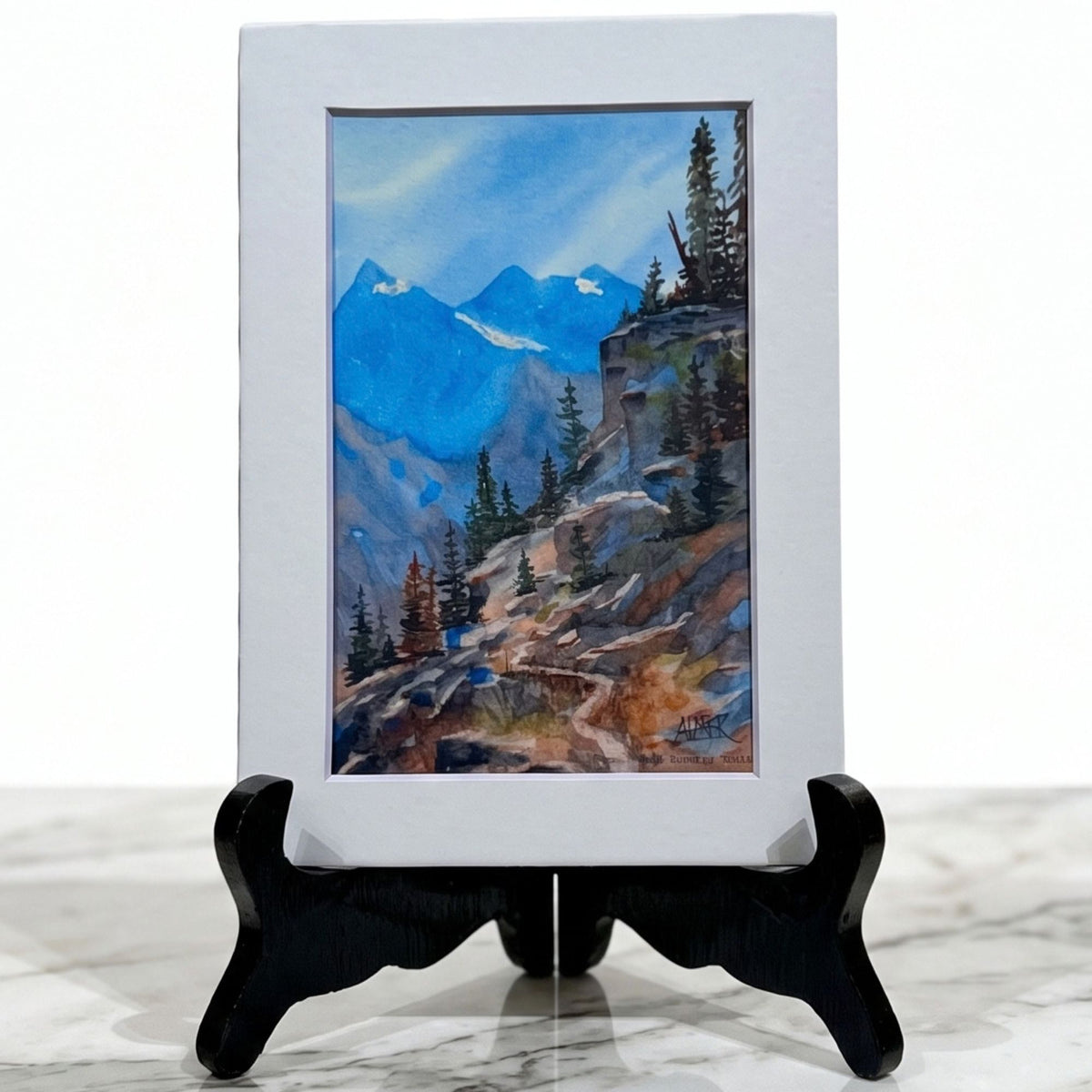 Discover high-altitude tranquility with Stark Mountain Studio's matted 5x7 print of a Bobbe Almer watercolor hiking trail in Western Montana's rugged mountains.