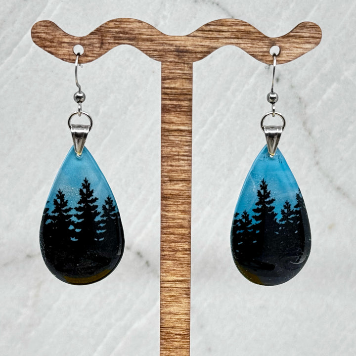 Pair of Large Teardrop Earrings with Trees, by Bitterroot Shining Creations, featuring tree silhouettes against a sparkly light blue polymer clay background (3-4 trees), hanging