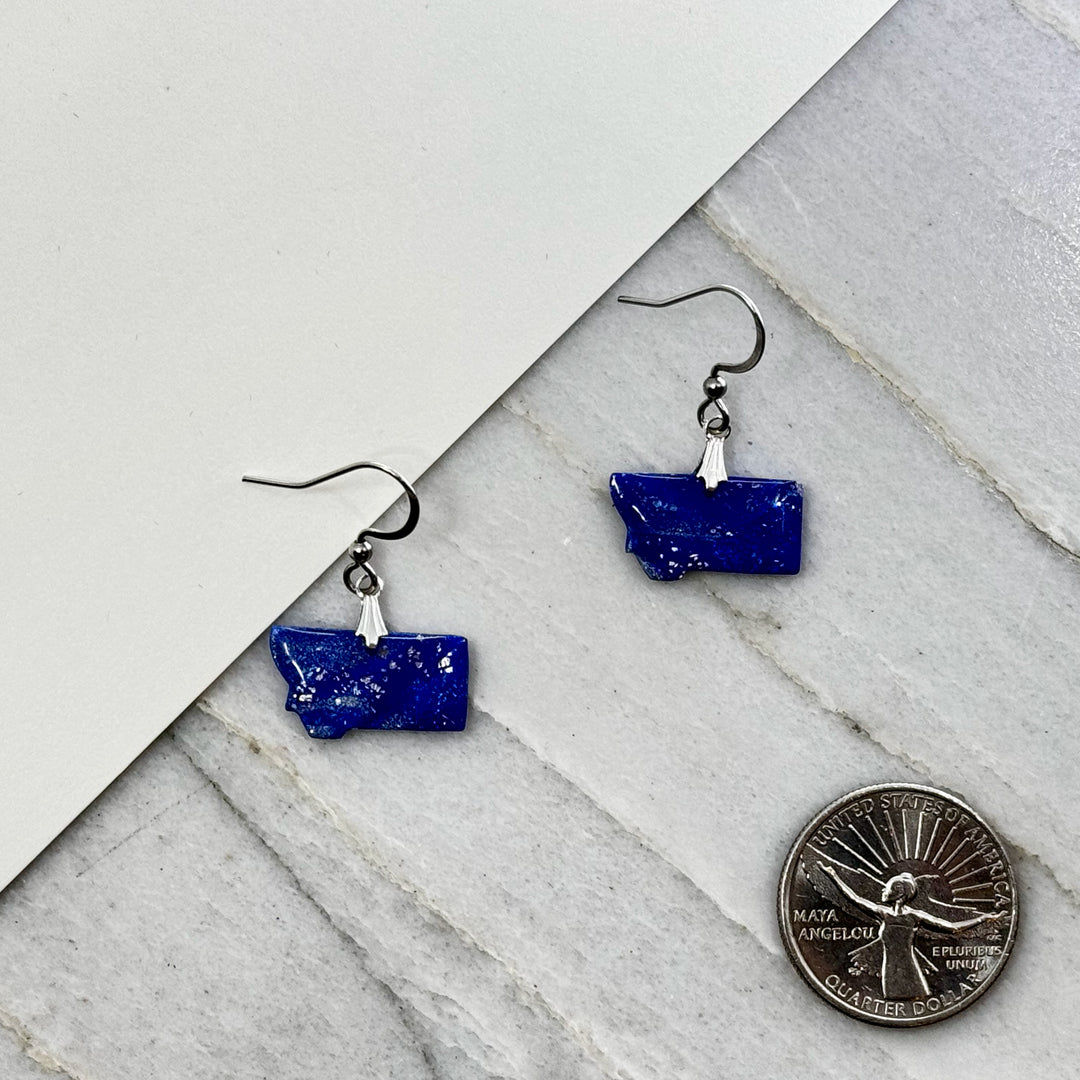 Pair of small, polymer clay Montana Earrings by Bitterroot Shining Creations in assorted sparkly colors (blue and silver), with scale