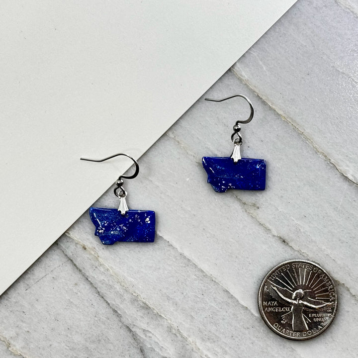 Pair of small, polymer clay Montana Earrings by Bitterroot Shining Creations in assorted sparkly colors (blue and silver), with scale