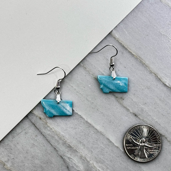 Pair of small, polymer clay Montana Earrings by Bitterroot Shining Creations in assorted sparkly colors (light blue), with scale