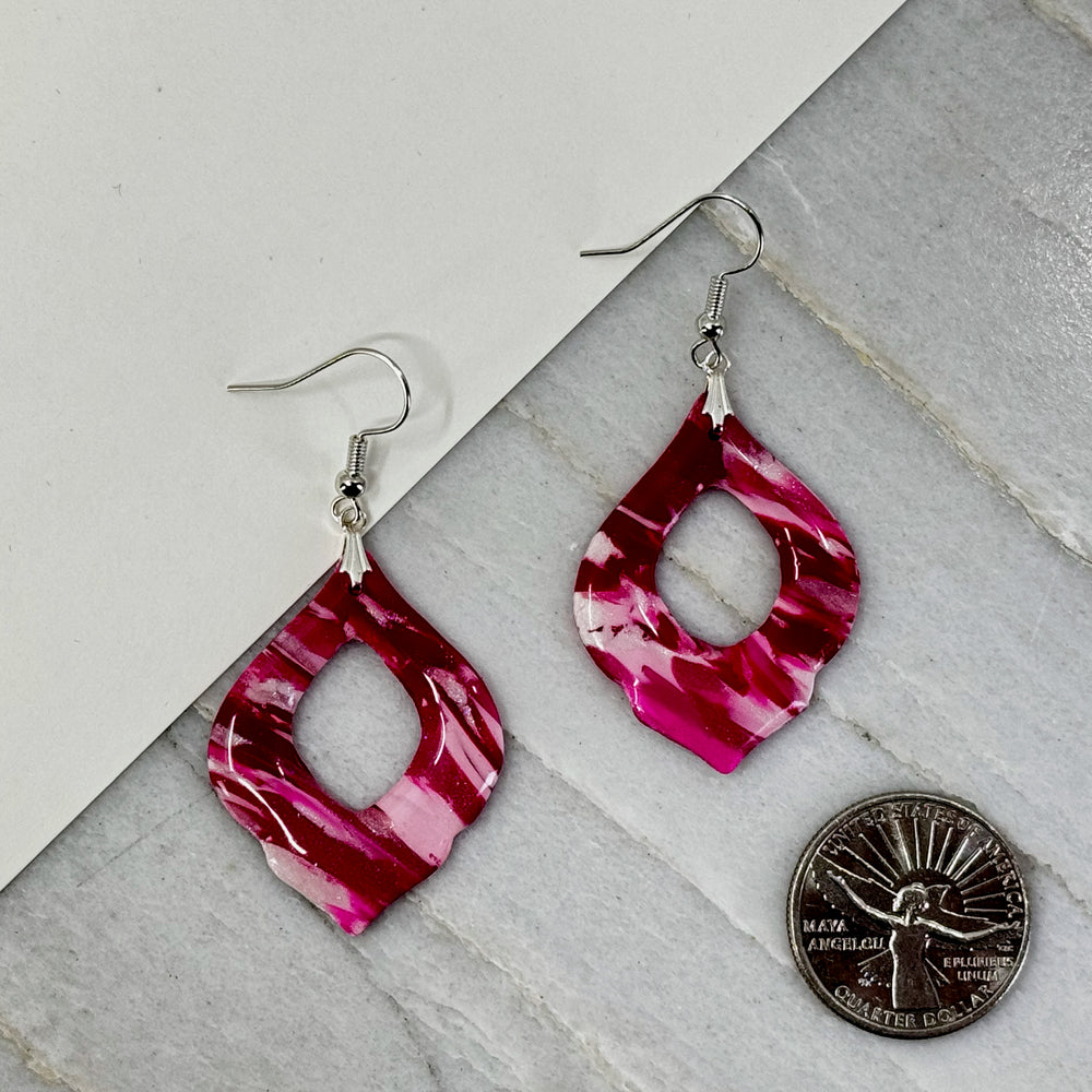 Pair of Pink and Red Arabesquee Earrings by Bitterroot Shining Creations, featuring marbleized pink and red polymer clay, with scale
