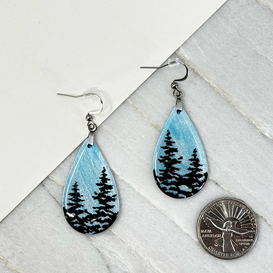 Pair of Large Teardrop Earrings with Trees, by Bitterroot Shining Creations, featuring tree silhouettes against a sparkly light blue polymer clay background (2 trees), with scale