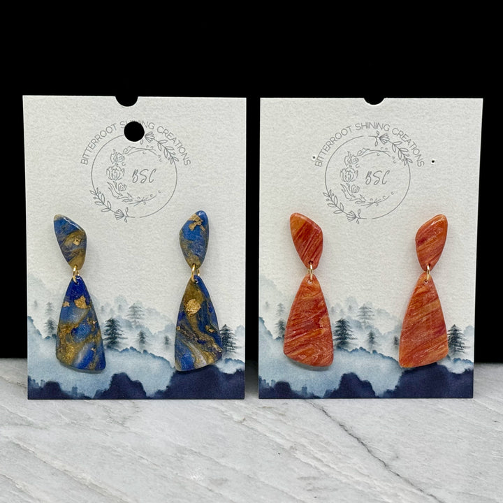 Two pairs of Abstract Earrings by Bitterroot Shining Creations (blue and gold or orange), on cards