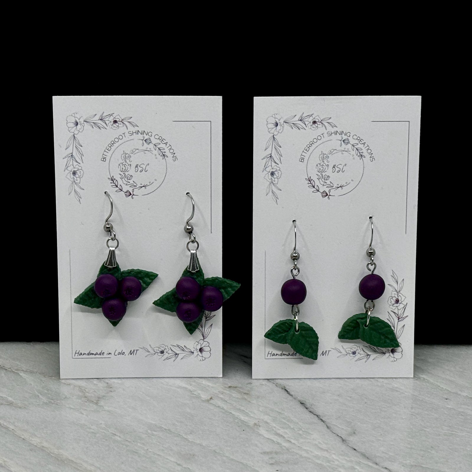 Pair of polymer clay Huckleberry Earrings on stainless steel ear wires by Bitterroot Shining Creations (single or triple berry design), on cards