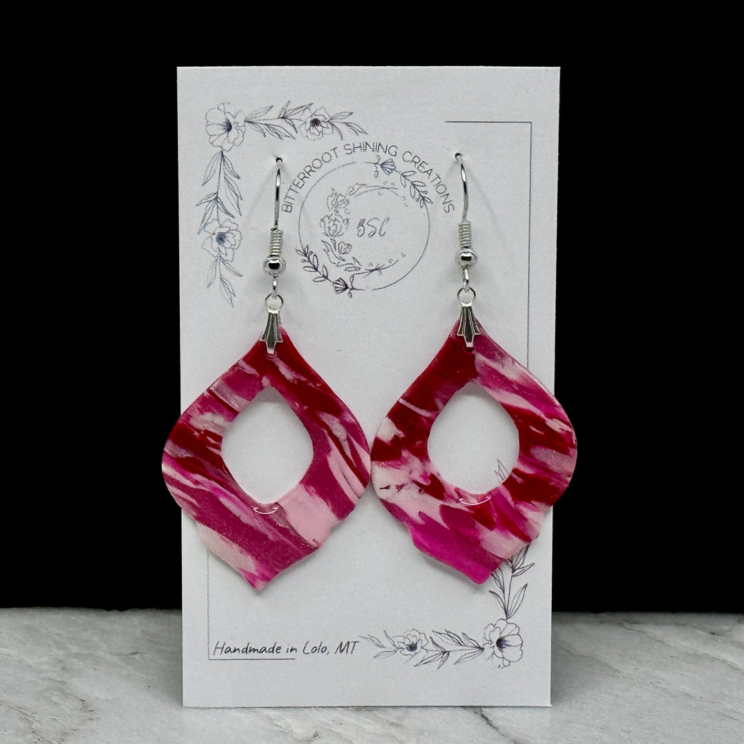 Pair of Pink and Red Arabesquee Earrings by Bitterroot Shining Creations, featuring marbleized pink and red polymer clay, on card