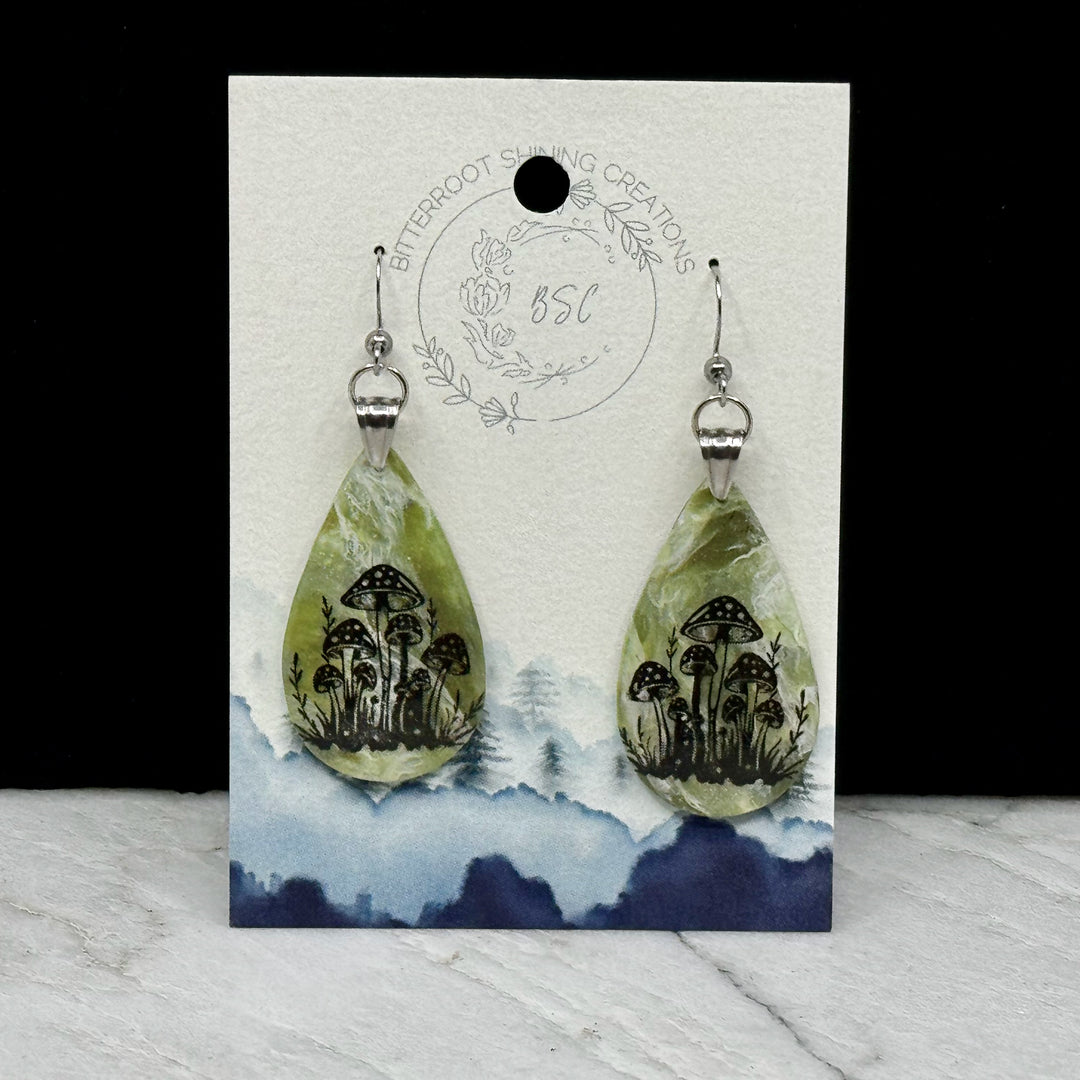 Pair of Large Teardrop Earrings with Mushrooms by Bitterroot Shining Creations, featuring a cluster of black mushrooms against a marbleized green polymer clay backdrop, on card
