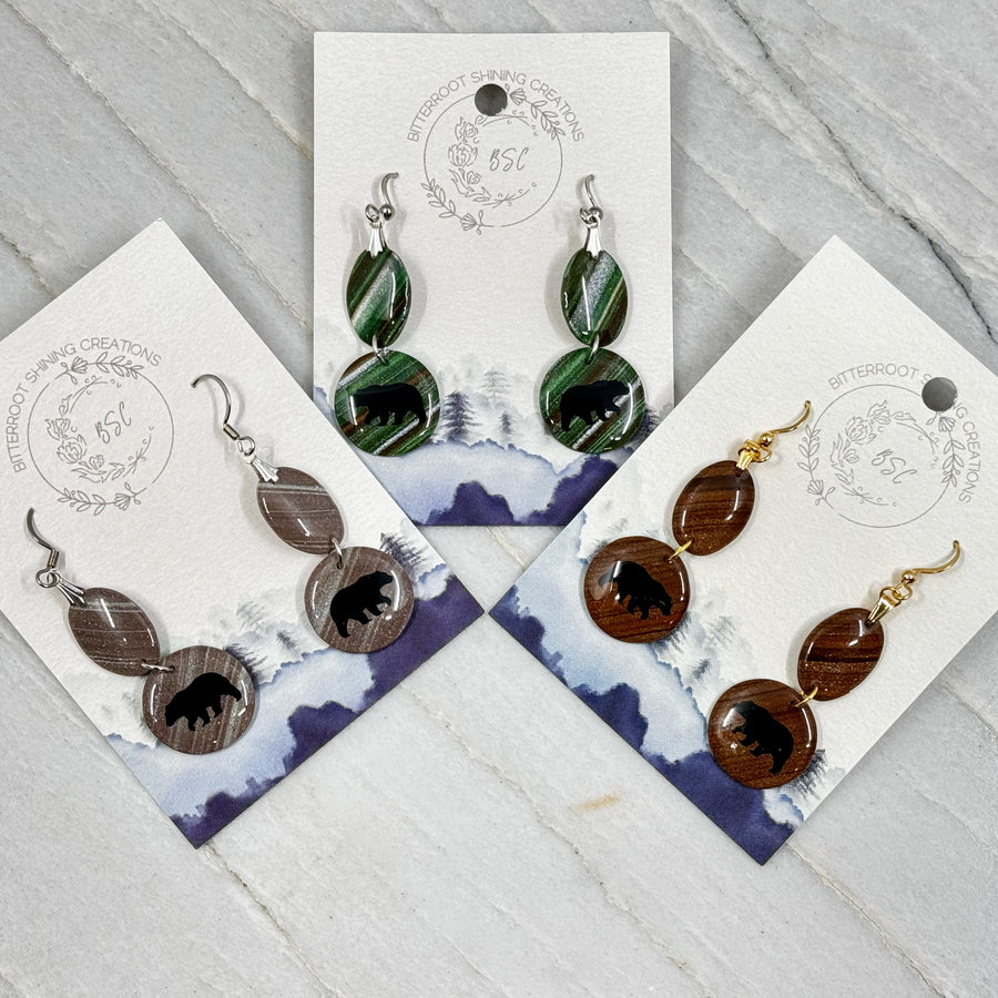 3 pairs of Small Dangle Earrings with Bears by Bitterroot Shining Creations, featuring double drop polymer clay in in various colors with a bear silhouette on the bottom drop (brown, green, and taupe), on cards