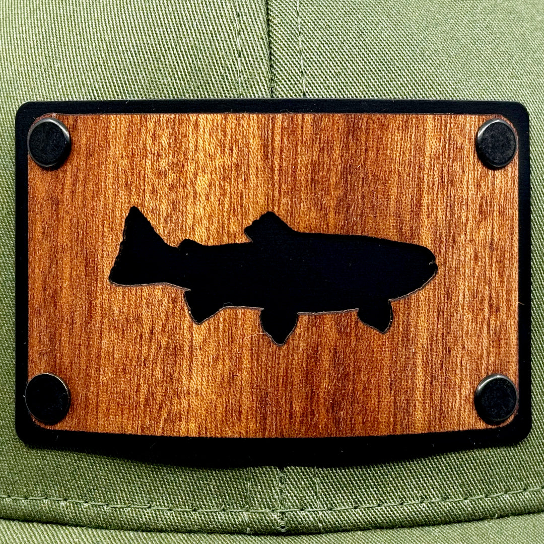 Last Best Supply Co's Olive Green & Khaki Mesh Mahogany Patchplate Trout Silhouetted Trucker Hat, featuring the silhouette of a trout cut out of mahogany against a black metal patch (patch detail)