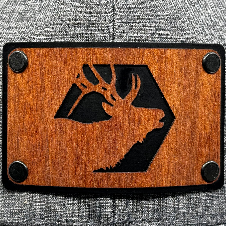 Last Best Supply Co's Mahogany Elk & Metal Patch Flexfit Trucker Hat, featuring an elk silhouette cut out of mahogany set against a black metal patch riveted to a grey and black trucker hat (patch detail)