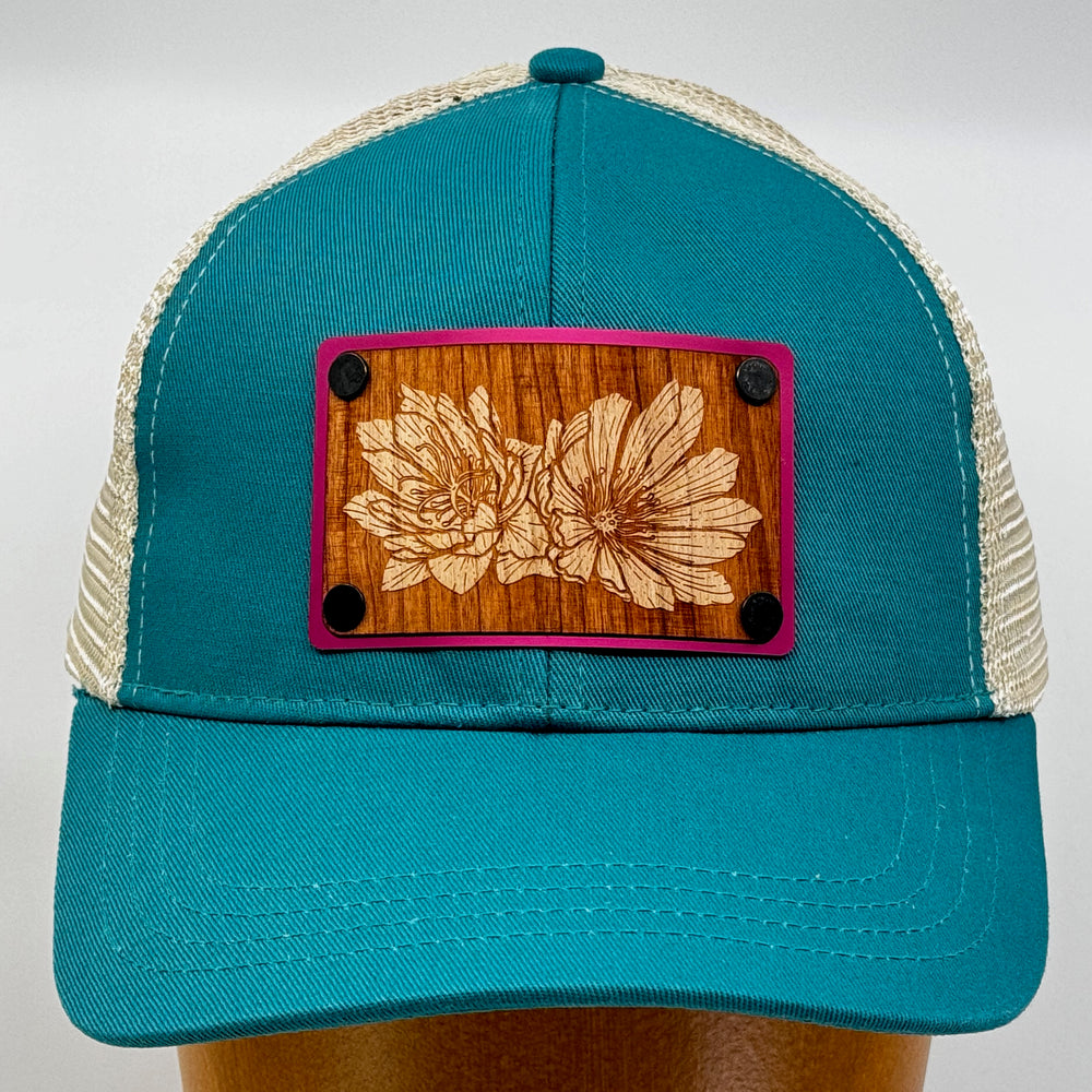 Last Best Supply Co's Bitterroot Cherry & Pink Metal Patch on Evergreen Eco Trucker Hat, featuring a cherry wood patch engraved with bitterroot flowers (front view)