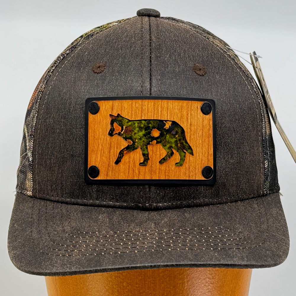 Last Best Supply Co's Cherry Wood & Green Copper Wolf Patch Plate Mossy Oak Trucker Hat (front view)