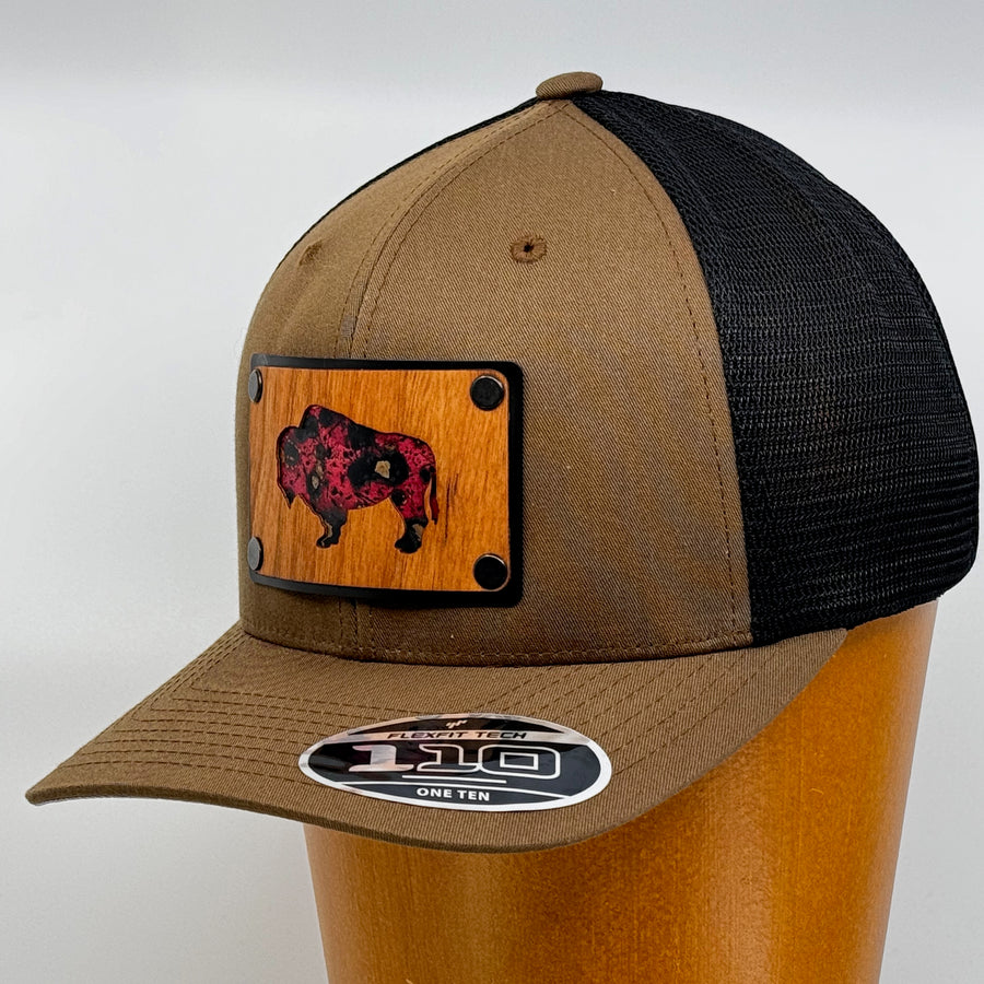 Last Best Supply Co's Cherry Wood & Red Copper Bison Coyote Brown & Black Trucker Hat, featuring an oxidized copper bison silhouette cut out of cherry wood and set against a black metal patch (3/4 view)