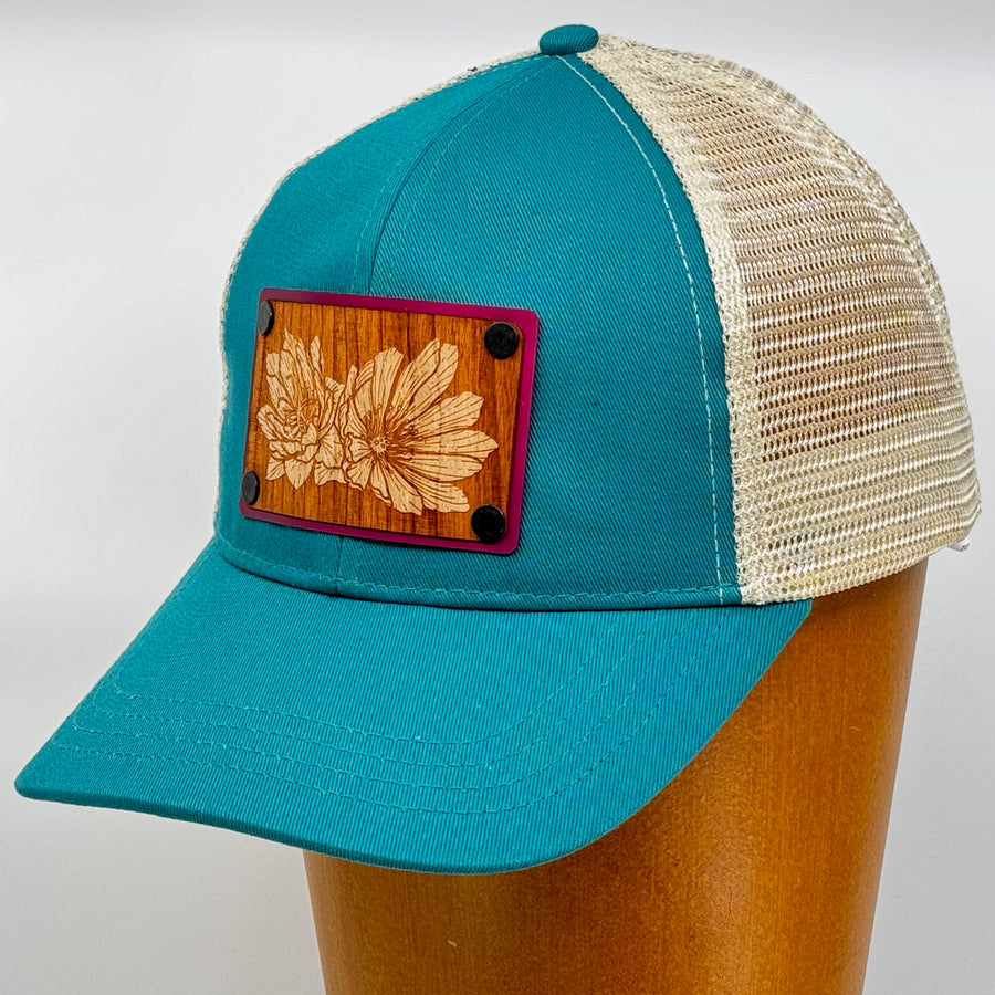 Last Best Supply Co's Bitterroot Cherry & Pink Metal Patch on Evergreen Eco Trucker Hat, featuring a cherry wood patch engraved with bitterroot flowers (3/4 view)