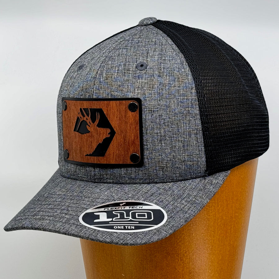 Last Best Supply Co's Mahogany Elk & Metal Patch Flexfit Trucker Hat, featuring an elk silhouette cut out of mahogany set against a black metal patch riveted to a grey and black trucker hat (3/4 view)