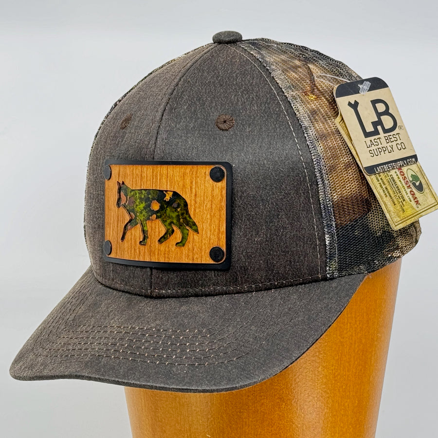 Last Best Supply Co's Cherry Wood & Green Copper Wolf Patch Plate Mossy Oak Trucker Hat (3/4 view)