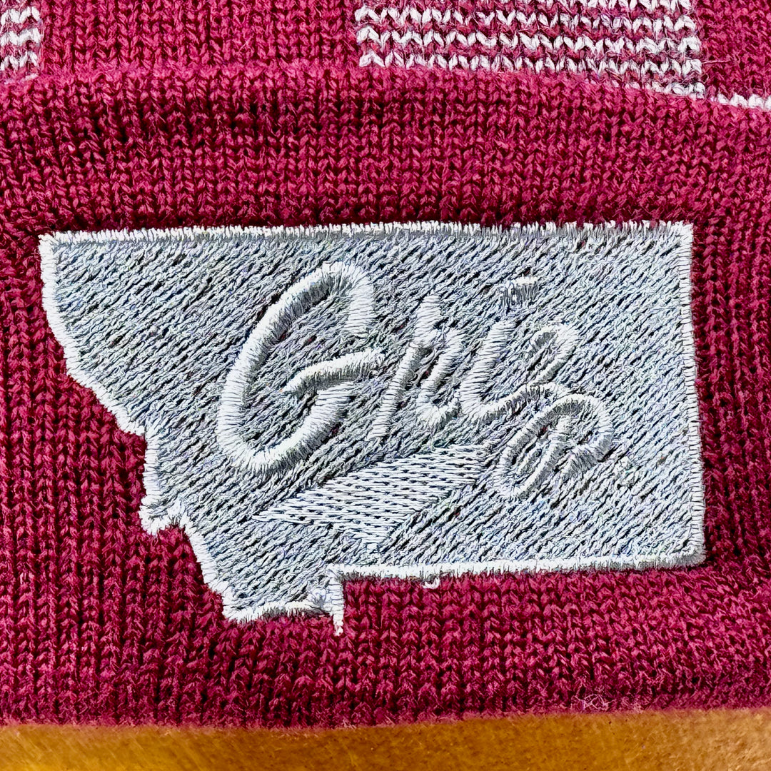 Blue Peaks Creative's grey and maroon USA-Made Plaid Beanie embroidered with the University of MT Griz Script over the state of Montana in silver (detail)