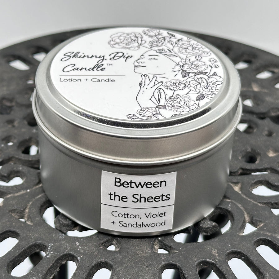 4 oz. tin of Skinny Dip Candle's Between the Sheets (cotton, violet & sandalwood) Lotion + Candle, front