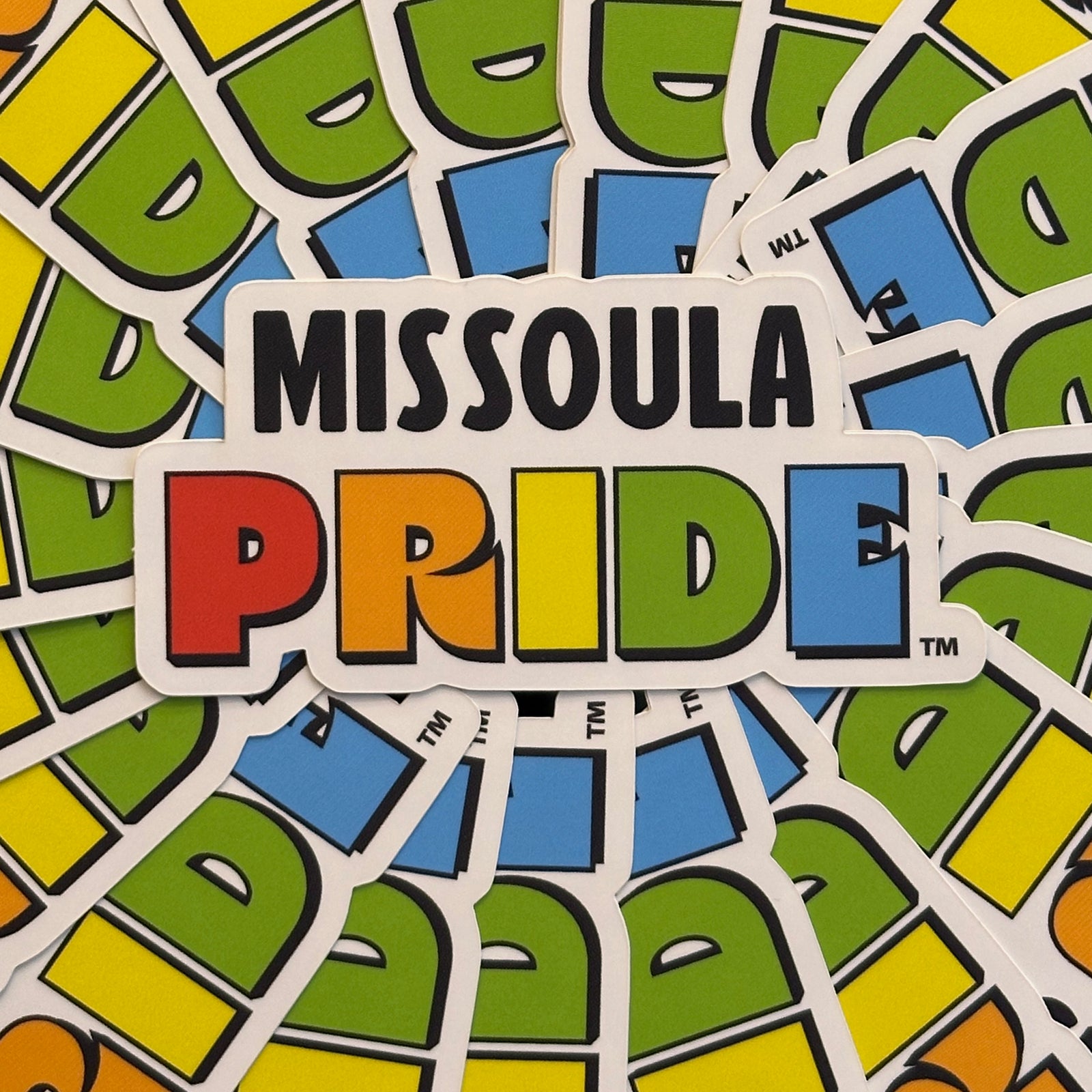 Circled group of Missoula PRIDE stickers with "PRIDE" in rainbow tones on a white background, closeup