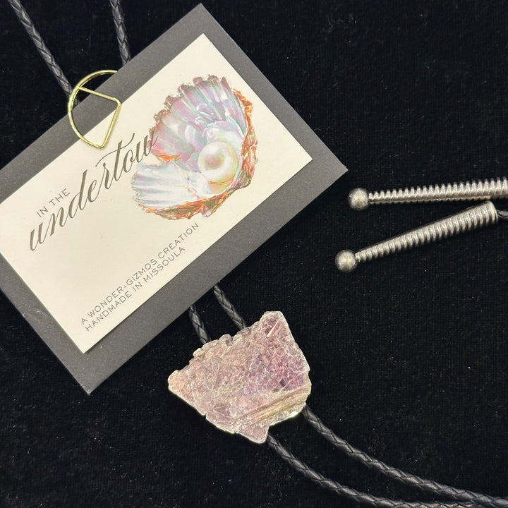 A lepidolite bolo tie on a black leather cord with metal tips made by In the Undertow