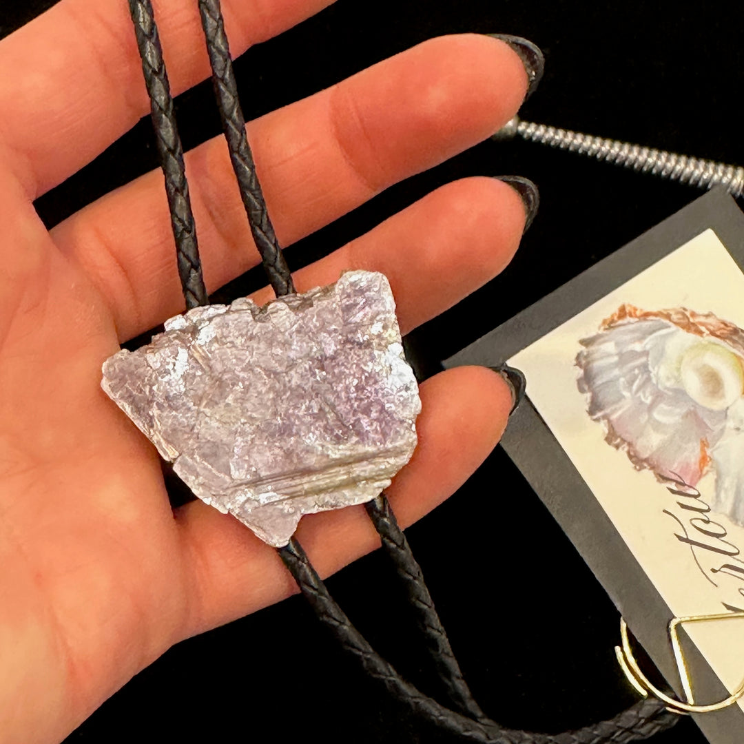 A close up of a hand holding a Lepidolite bolo tie