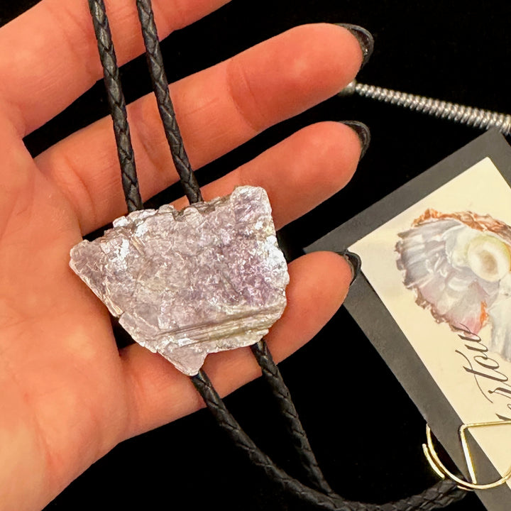 A close up of a hand holding a Lepidolite bolo tie