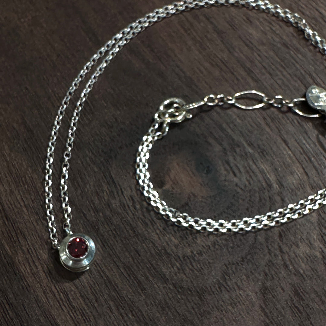 A cubic zirconia gemstone colored deep garnet red for a January Birthstone Necklace, set in sterling silver on a dark wood background