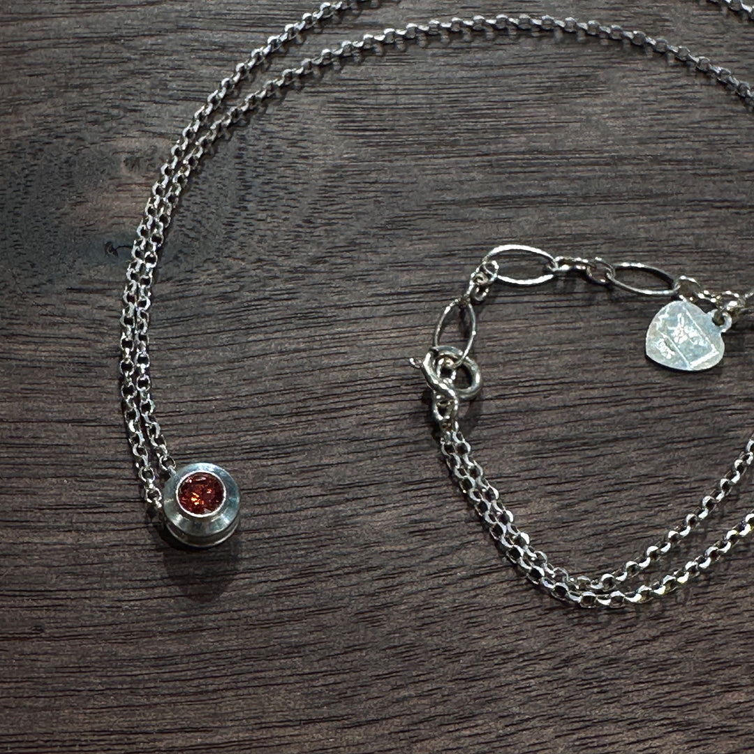 A cubic zirconia gemstone colored stunning Ruby red for a July Birthstone Necklace, set in sterling silver on a dark wood background