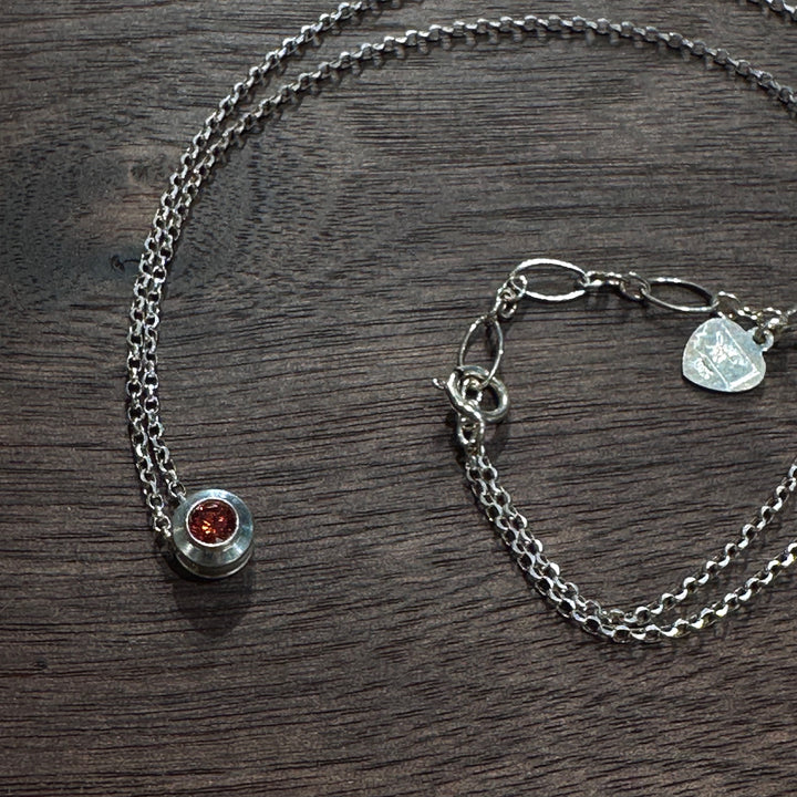 A cubic zirconia gemstone colored stunning Ruby red for a July Birthstone Necklace, set in sterling silver on a dark wood background