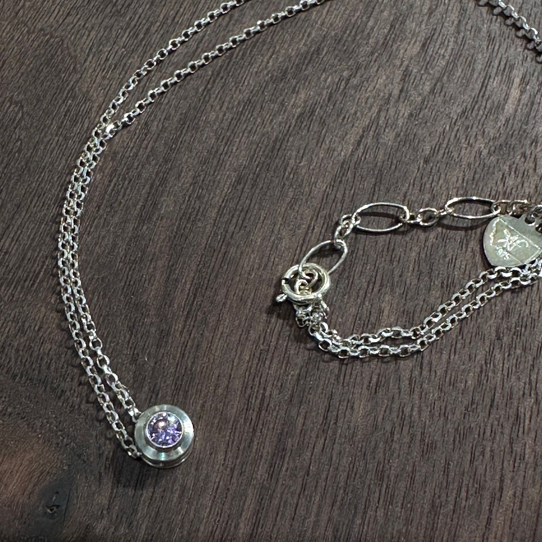 A cubic zirconia gemstone colored Lovely light purple Alexandrite  for a June Birthstone Necklace, set in sterling silver on a dark wood background