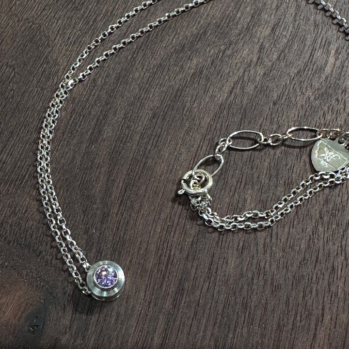 A cubic zirconia gemstone colored Lovely light purple Alexandrite  for a June Birthstone Necklace, set in sterling silver on a dark wood background
