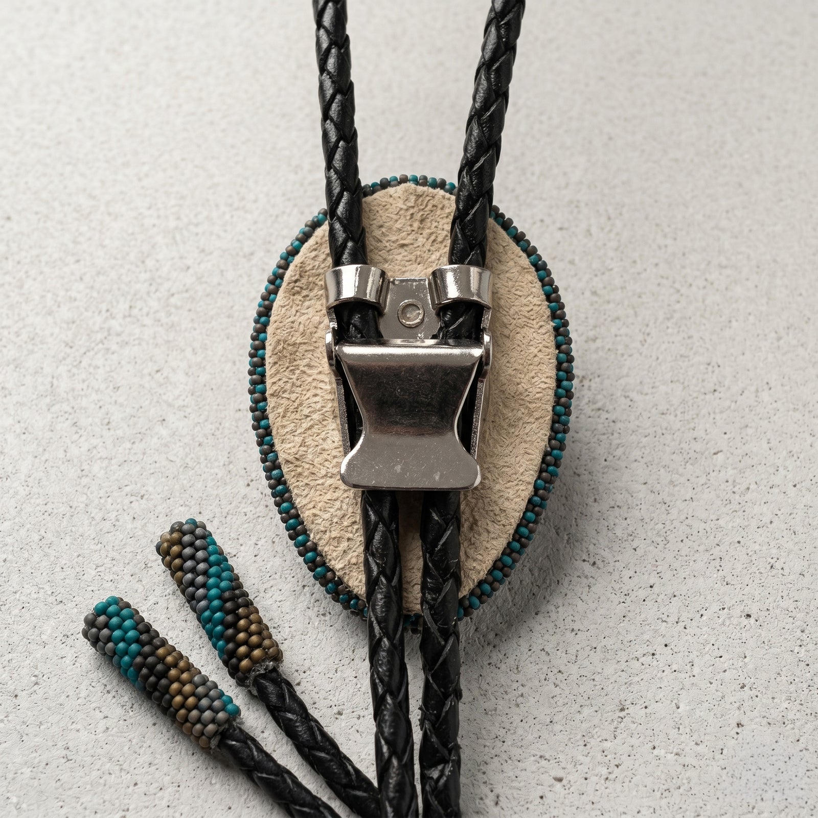 Bolo tie with black and teal braided cord on a textured gray background