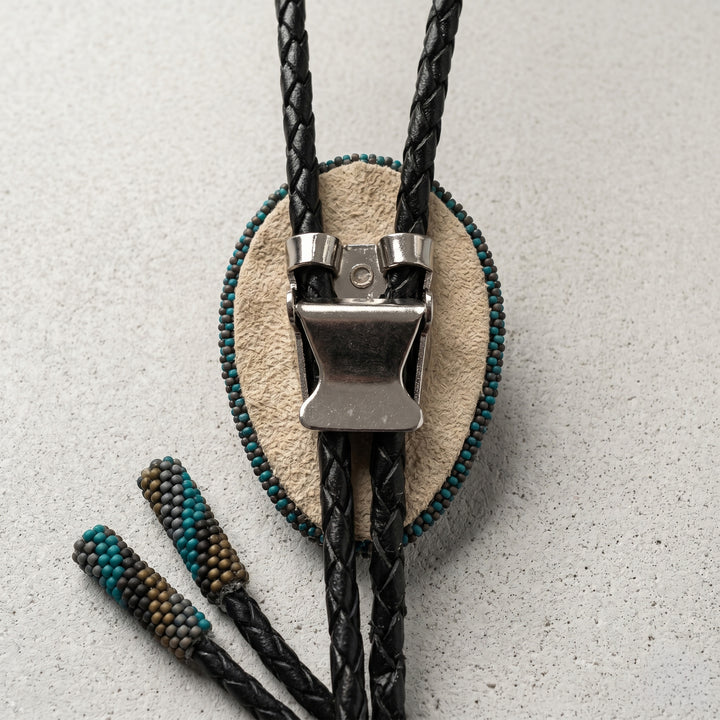 Bolo tie with black and teal braided cord on a textured gray background