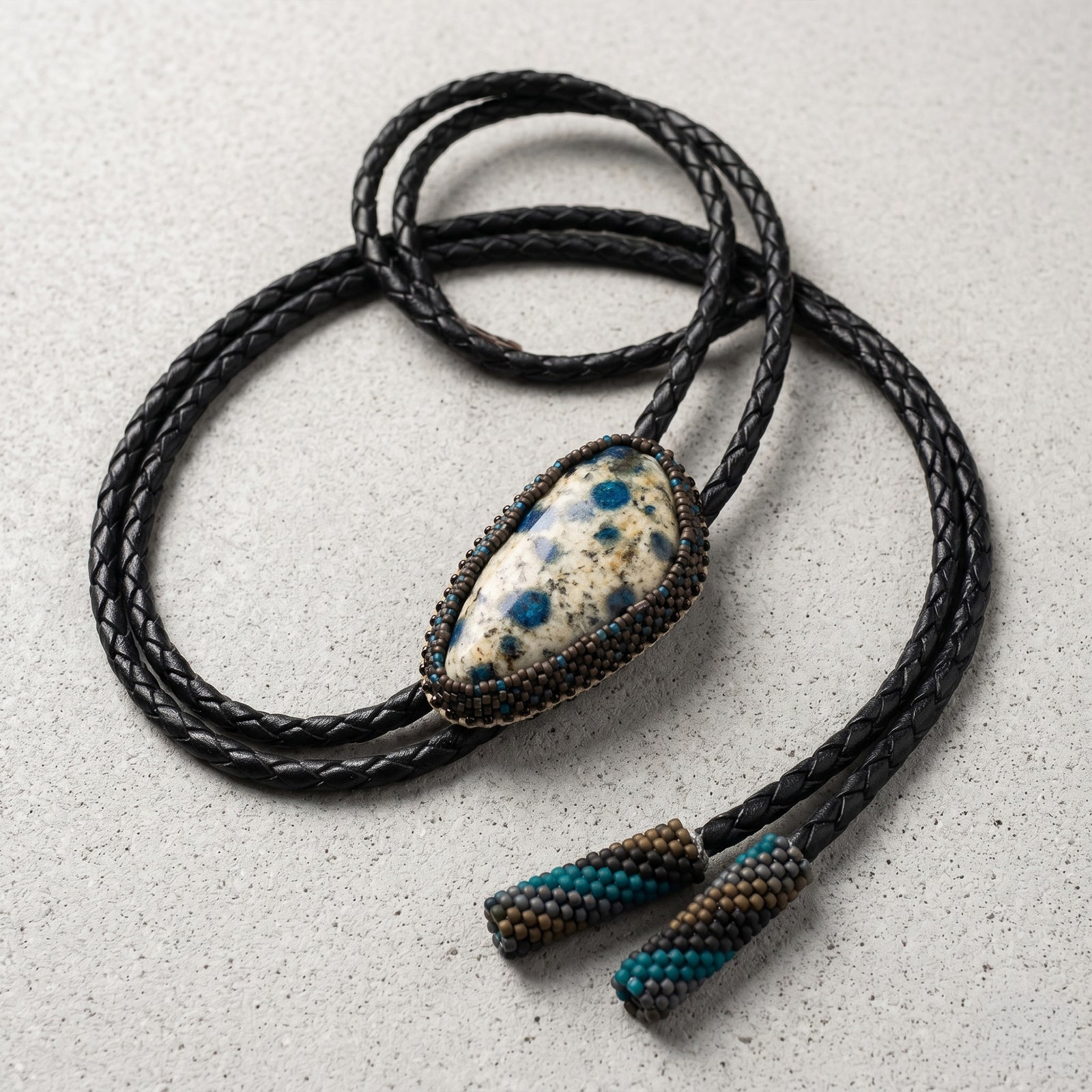 Black braided leather necklace with a stone pendant on a light gray surface