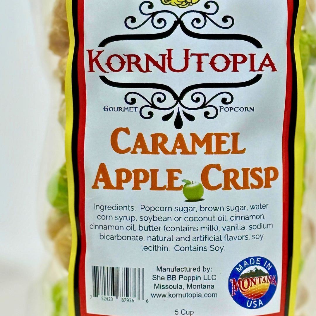 A close-up of a Korn Utopia Gourmet Popcorn bag labeled Caramel Apple Crisp, showing the front packaging with product name, ingredients, barcode, and a Made in Montana USA seal.