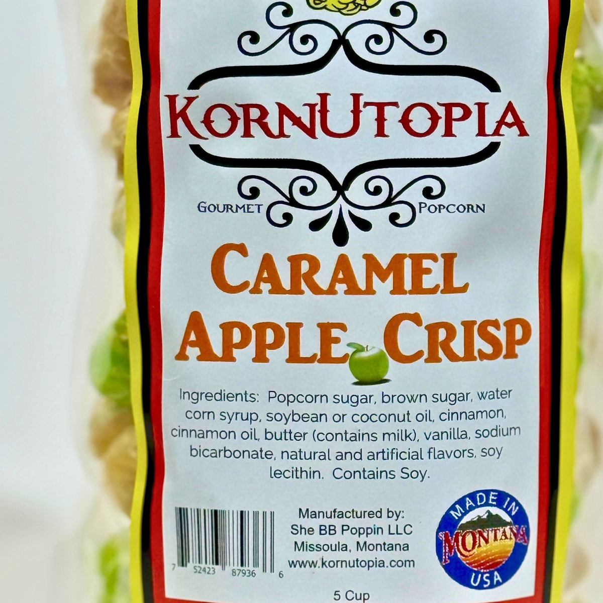 A close-up of a Korn Utopia Gourmet Popcorn bag labeled Caramel Apple Crisp, showing the front packaging with product name, ingredients, barcode, and a Made in Montana USA seal.