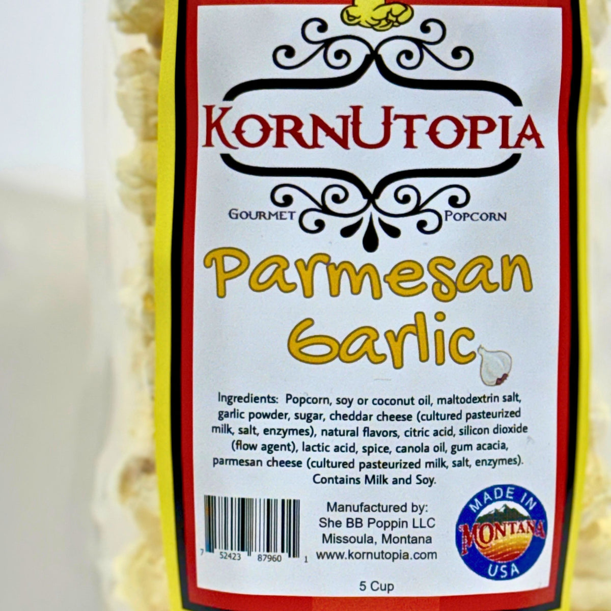 A close-up of a corn package label reading Kornutopia Gourmet Popcorn Parmesan Garlic, with a white label, red and yellow text, and a yellow corn cob illustration. The package itself appears mostly out of frame, with the label filling most of the image. Made in Montana USA
