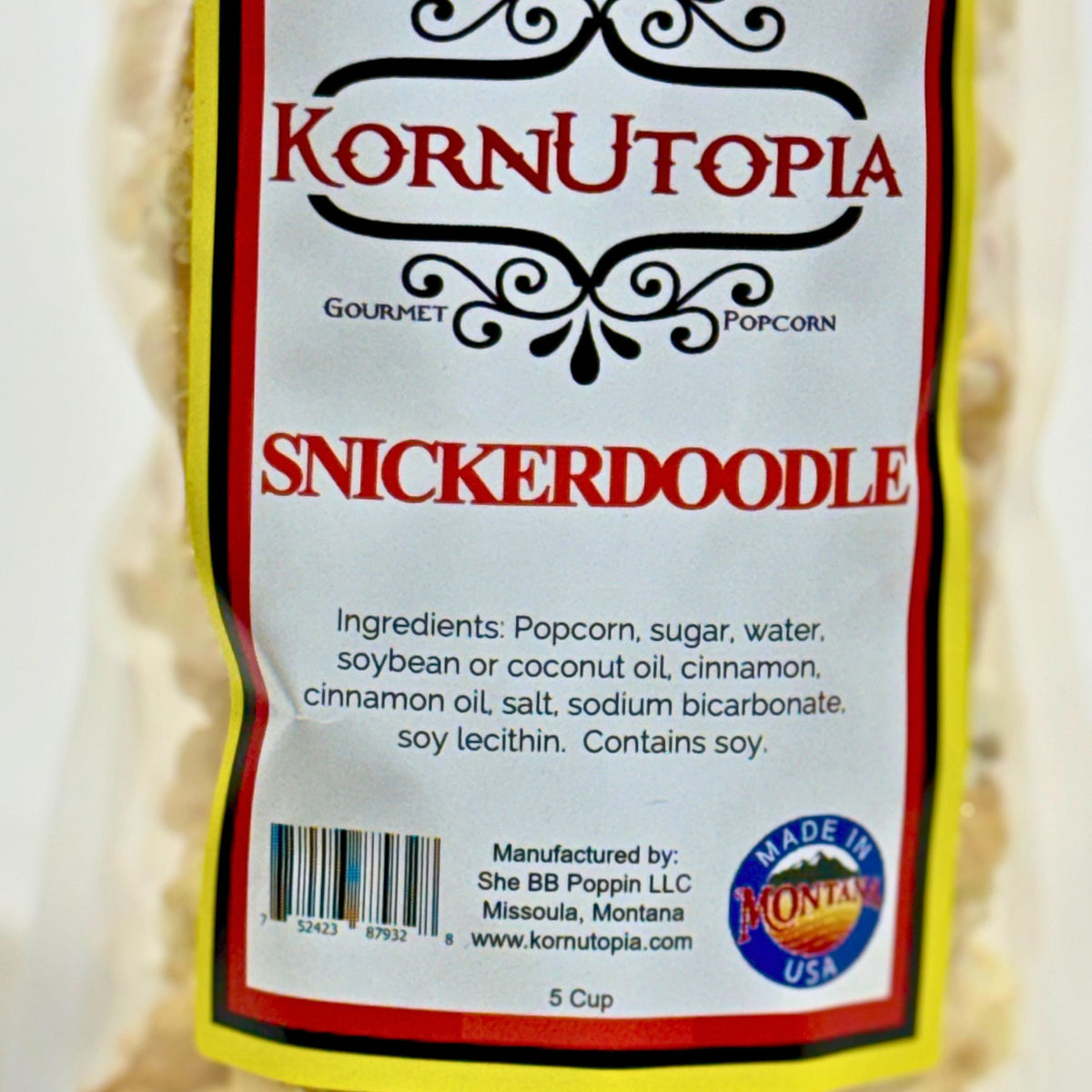 A close-up of a bag of Kornutoпия Snickerdoodle Gourmet Popcorn, showing the front label with red text, a yellow border, and a 'Made in Montana' logo.