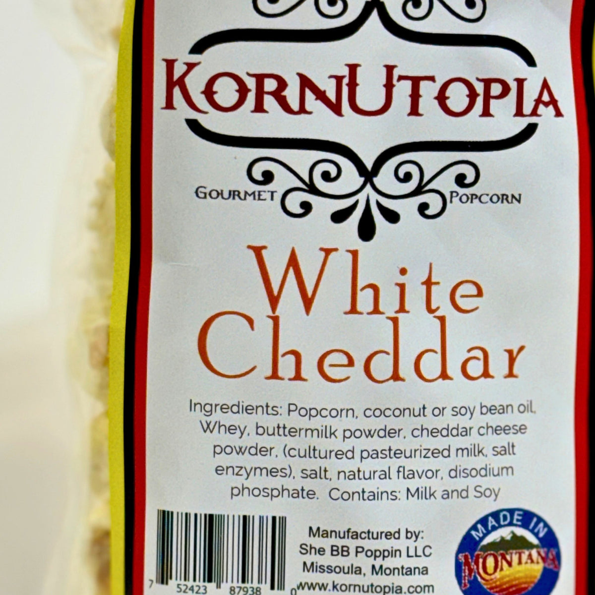 Close-up of a packaged snack bag labeled Kornutopia Gourmet Popcorn in White Cheddar flavor, with visible product text, barcode, and a Made in Montana badge