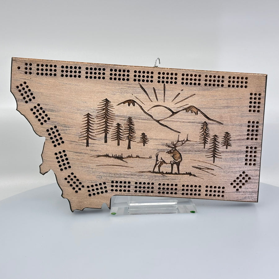 Knotty Pine Woodworks Handmade Montana Mountain Elk Cribbage Board Barn wood (front)--this made in Montana wooden cribbage board is shaped like the outline of the state of Montana, in natural weathered barn wood tones, and features an engraved elk standing in front of mountain peaks on the front.