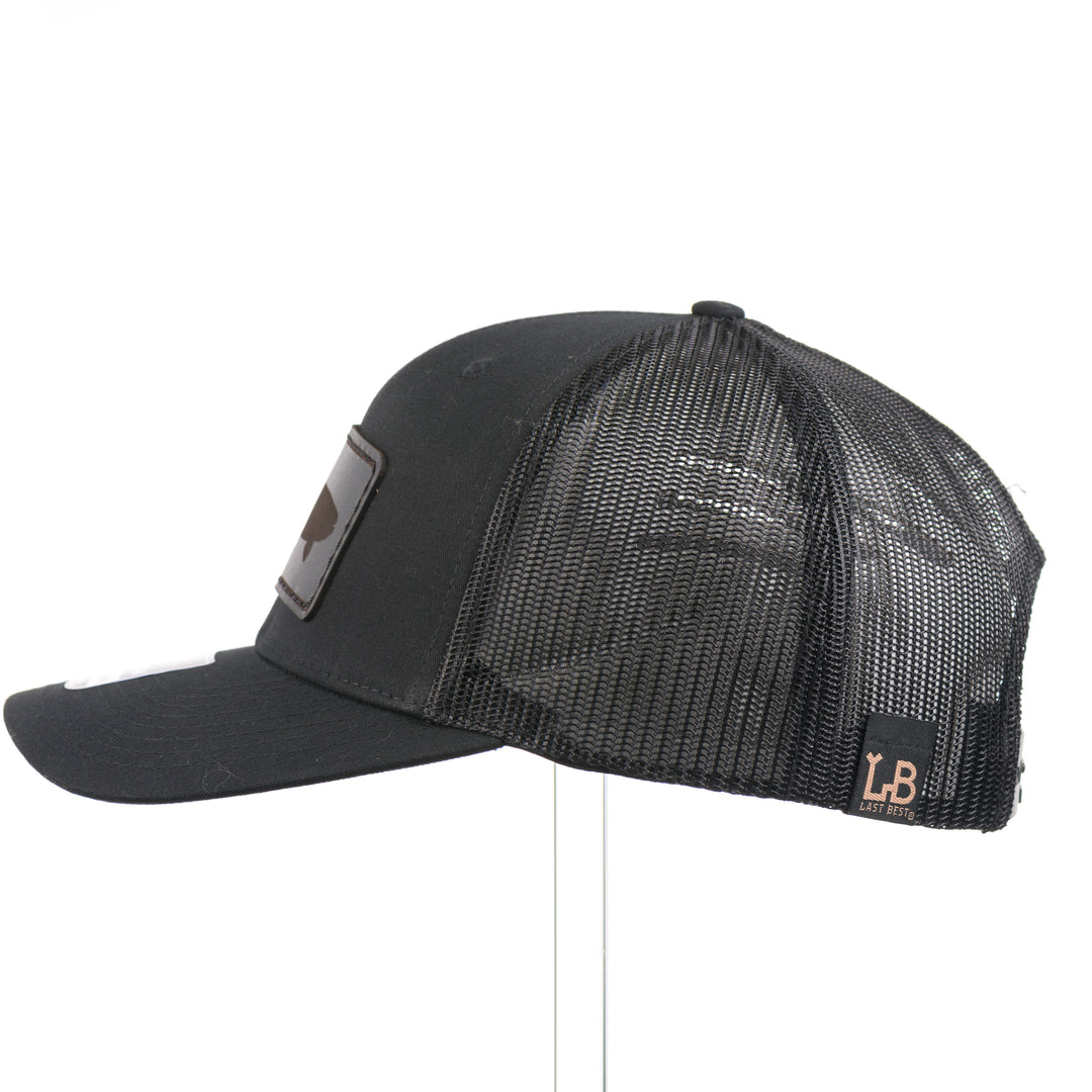The side of an all black Richardson trucker hat with a black leather trout rectangle patch thick stitched on with black thread—handmade in Montana, USA by Last Best Supply Co.