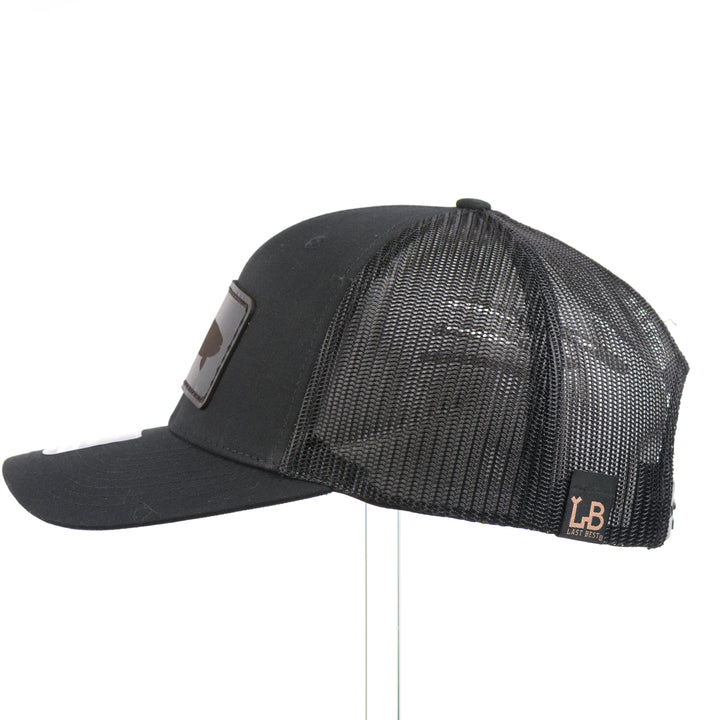 The side of an all black Richardson trucker hat with a black leather trout rectangle patch thick stitched on with black thread—handmade in Montana, USA by Last Best Supply Co.