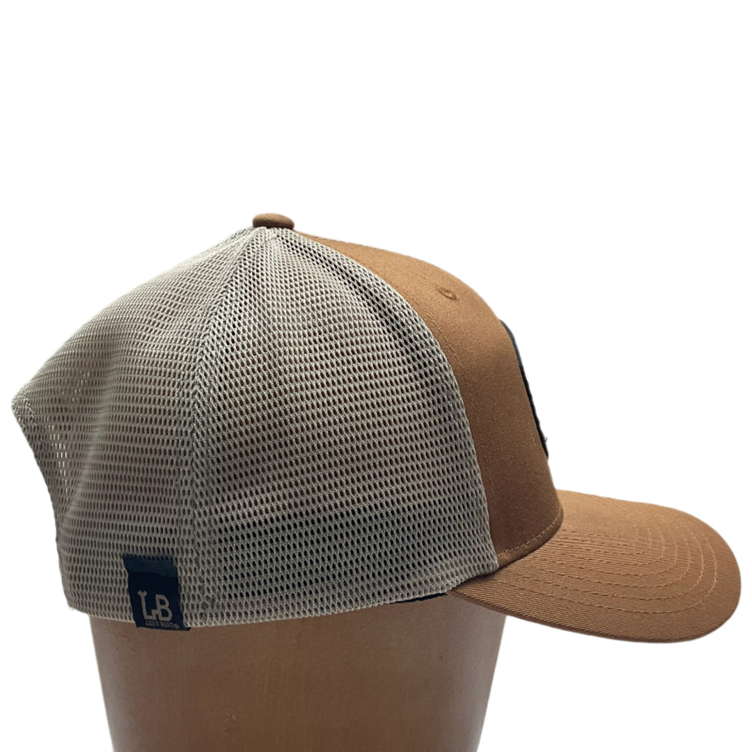 Side view of an Elk Hand Dyed Leather Patch Flexfit Hat, featuring a hexagonal hand-dyed leather patch etched with the silhouette of an elk and the letters “MT”, securely sewn to the structured front of a camel and cream colored Flexfit trucker hat—handmade in Montana, USA by Last Best Supply Co.