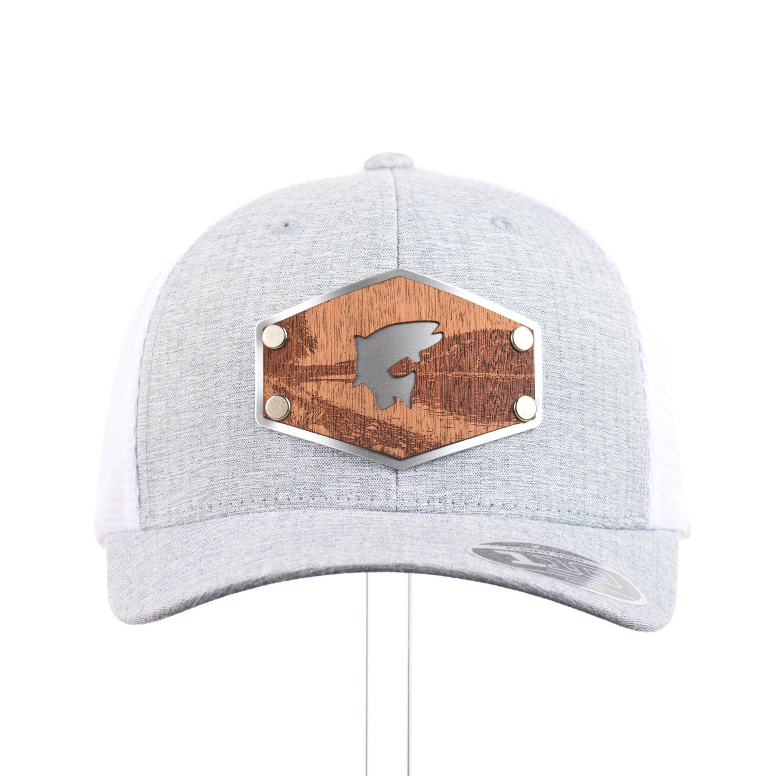The front of a Mahogany Wood Jumping Trout Patch Flexfit Trucker Hat, featuring a real mahogany wood patch cut into the silhouette of trees, mounted on an anodized aluminum plate and secured with silver rivets to a heathered silver and white Flexfit trucker hat—handmade in Montana, USA by Last Best Supply Co.