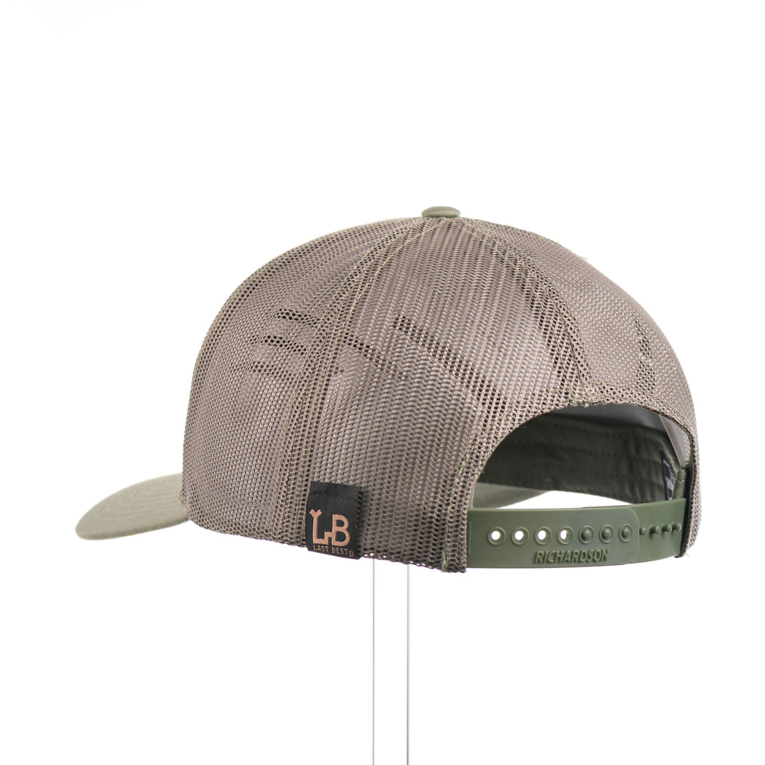 The back of an Etched Walnut Wood Mountain Patch Trucker Hat, featuring a real walnut wood patch cut into the shape of mountain peaks, mounted on a black anodized aluminum plate and secured with rivets to a loden green Richardson 112 trucker hat—handmade in Montana, USA by Last Best Supply Co.