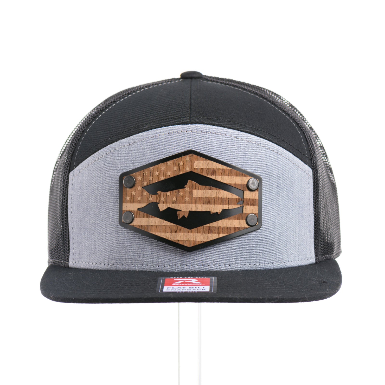 The front of a Walnut Wood Chinook Salmon American Flag Flat Bill Trucker Cap, featuring a real walnut wood veneer patch precision-cut into a hexagon, etched with an American flag with a Chinook salmon cut-out, laminated to a hexagonal black anodized aluminum plate, and riveted to a heather gray and black Richardson 168 flat bill trucker hat—handmade in Montana, USA by Last Best Supply Co.